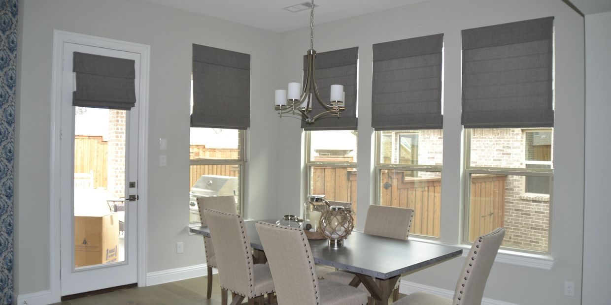 Modern dining room with gray roman shades and a metal chandelier.