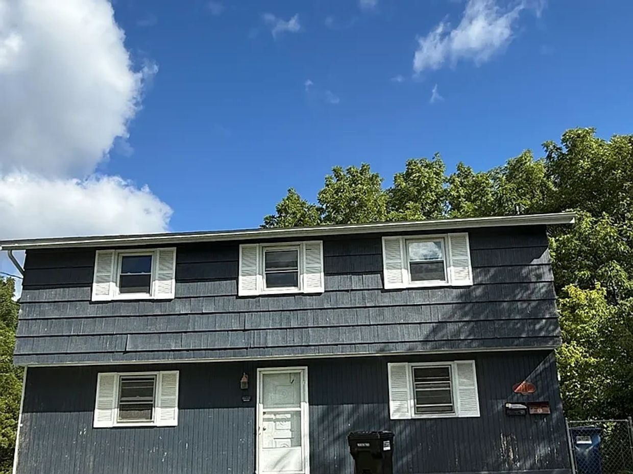 Dark blue two-story house with white shutters under a bright sky.