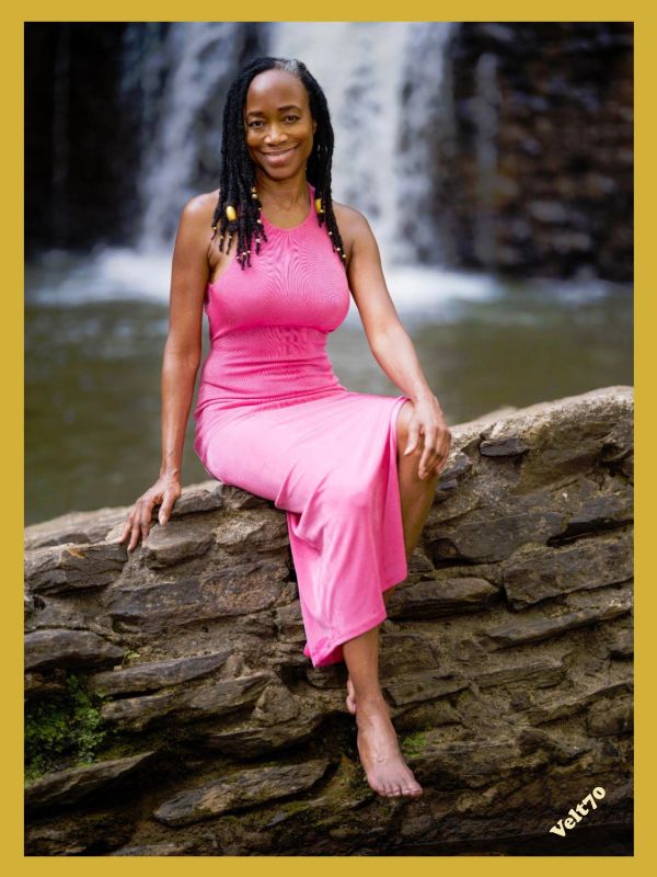 Woman in pink dress sitting by a waterfall.