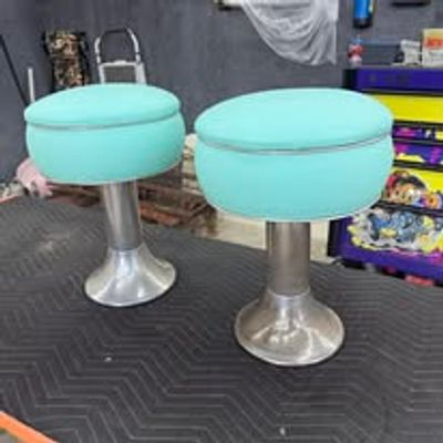 Two turquoise round stools with metallic bases on a black surface.