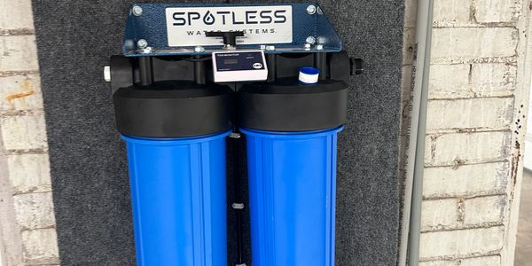 Spotless Water Systems filtration unit with two large blue canisters installed on a wall.