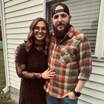 A smiling couple posing outside a house, showing affection.