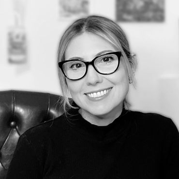 Smiling woman wearing glasses and a black top, seated on a leather chair.