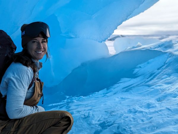 Smiling woman in winter gear near a large blue ice formation.