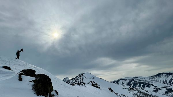 Person taking photo on snowy mountain under cloudy sky and sun.