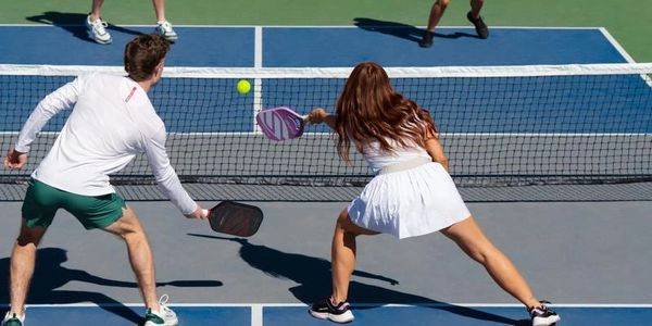 Two teams playing pickleball on a court, hitting the ball over the net.