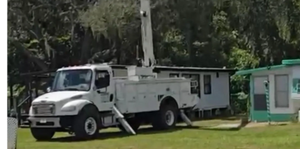 White utility truck with extended stabilizers parked on grass near residential buildings.