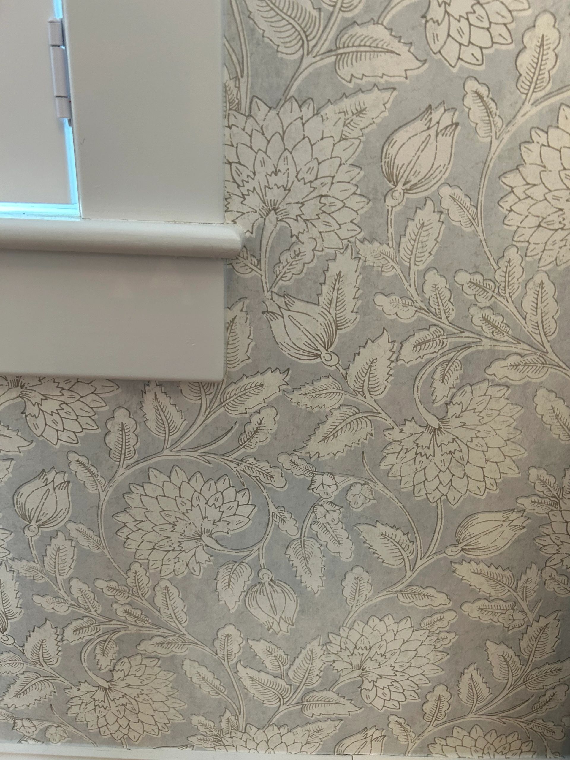 Close-up of grey floral wallpaper beside a white window frame.