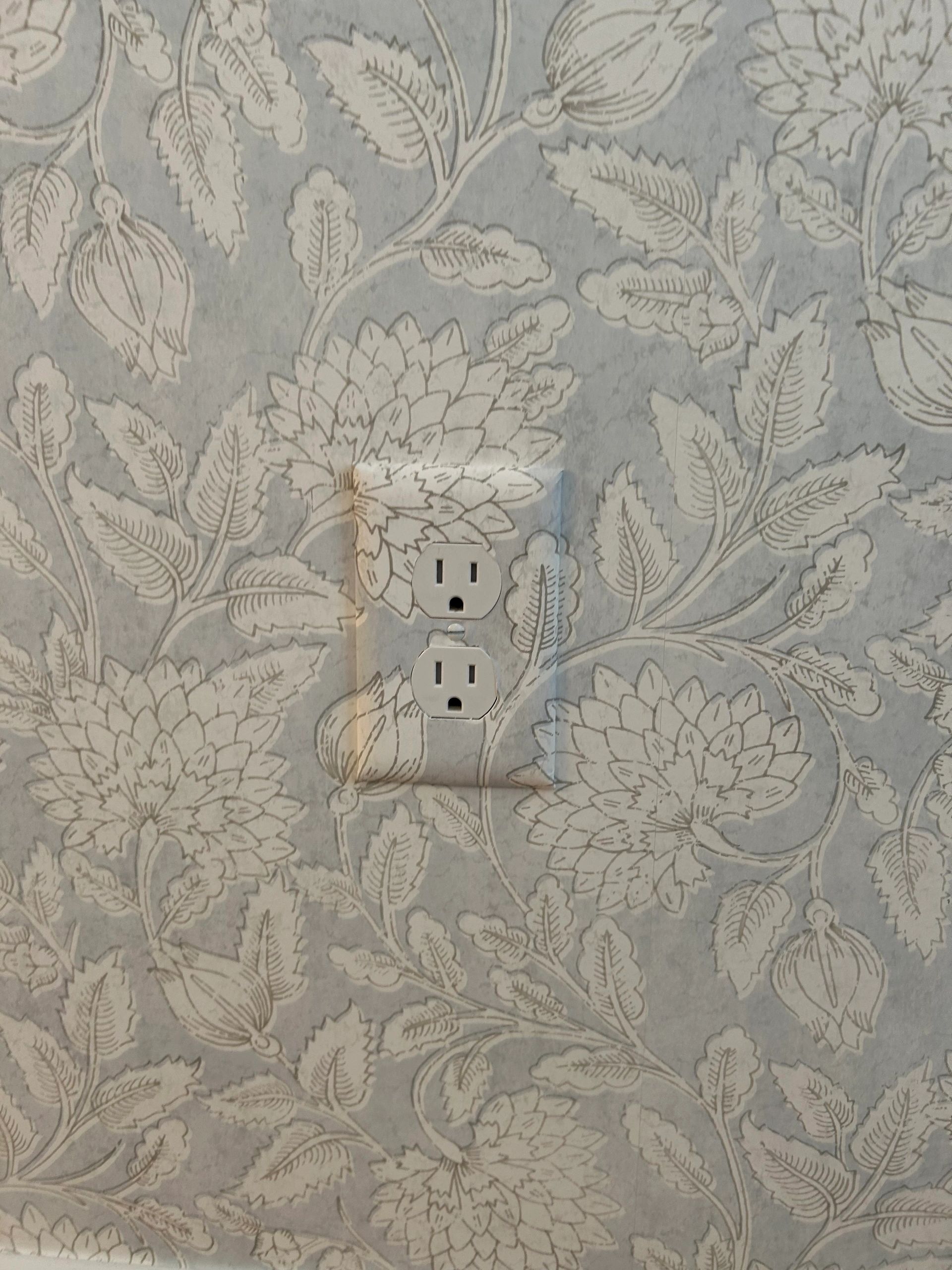 Floral patterned wallpaper with a white electrical outlet.