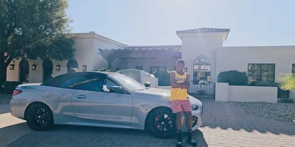 Young boy standing next to a silver convertible car in front of a house.