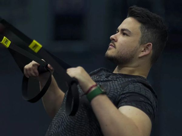 A focused individual performs a TRX suspension row in a gym environment, demonstrating proper form.