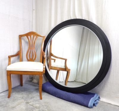 Wooden chair next to a large round mirror with black frame.