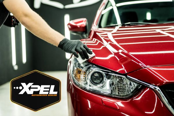 Person polishing a red car's headlight with XPEL authorized dealer logo.