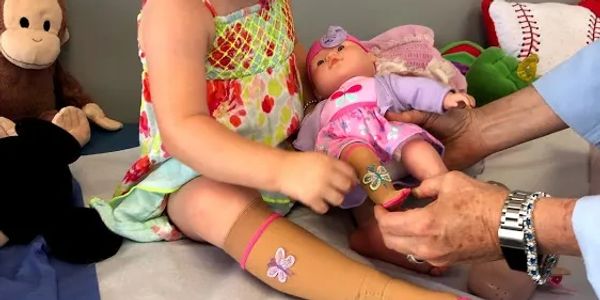 A young girl being handed a new doll by a medical professional