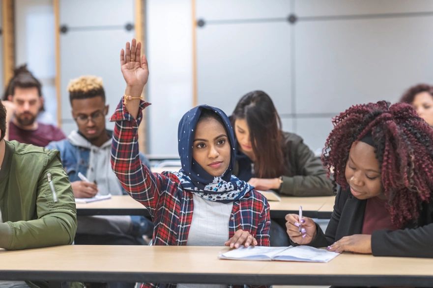 Student in hijab raising hand in classroom.
