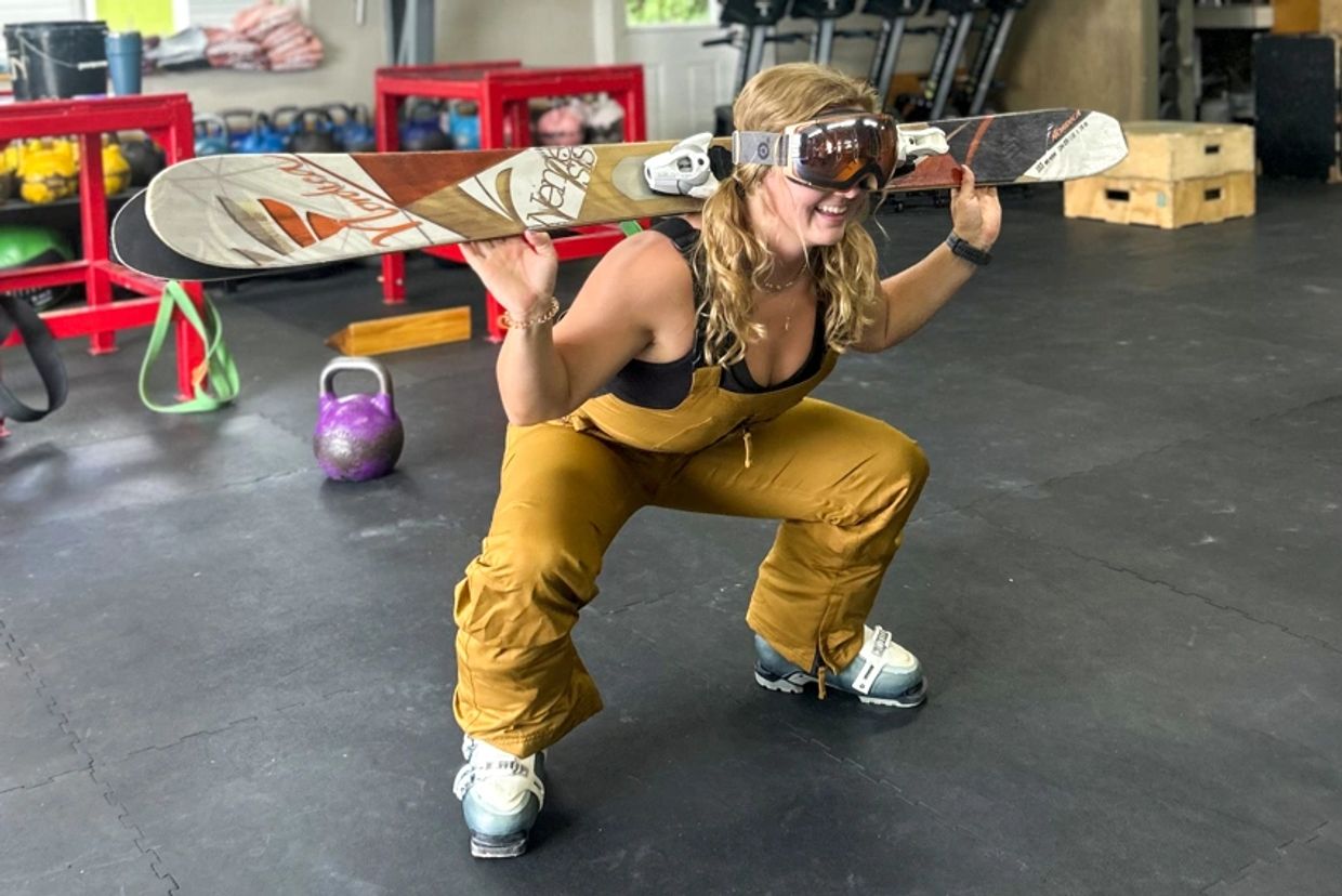 Coach Alexa squatting in the gym in ski gear.