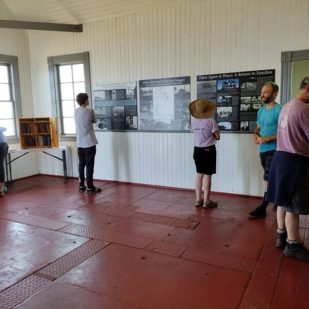 Visitors read historical panels in a small museum with red floors and white walls.