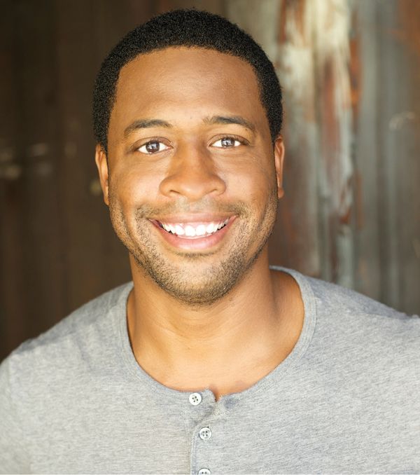 Smiling man wearing a gray shirt with buttons, looking at the camera.