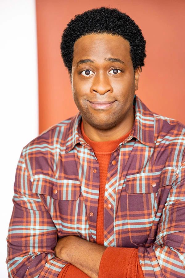 Man in a plaid shirt with a skeptical expression against a warm background.