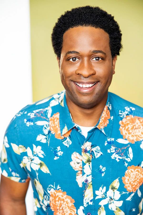 Smiling man in a blue floral shirt against a light background.