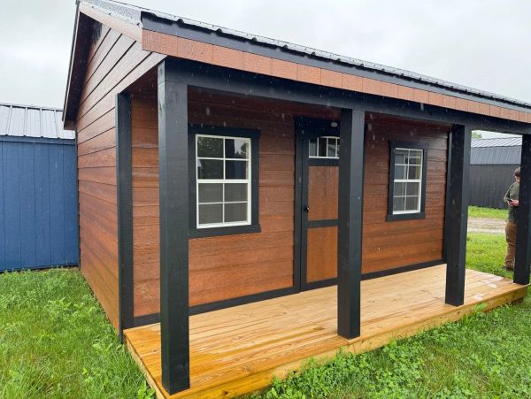Small wooden cabin with a porch on a grassy area.