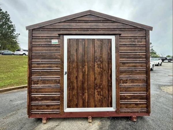 Small wooden shed with a centered door on a paved area.