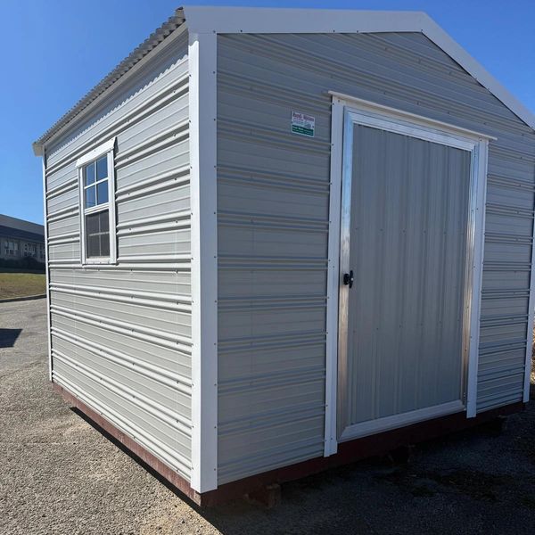 Metal storage shed with a window and a door under clear blue sky.
