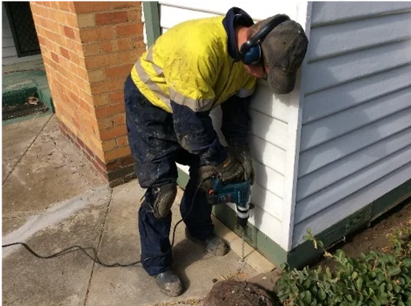Worker drilling into the foundation of a house.