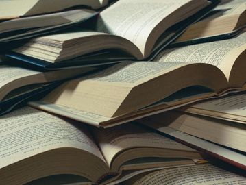 A pile of open books with visible text on their pages.