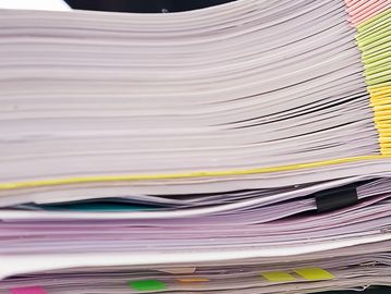 Close-up of large stacks of documents with colorful tabs and a pen.