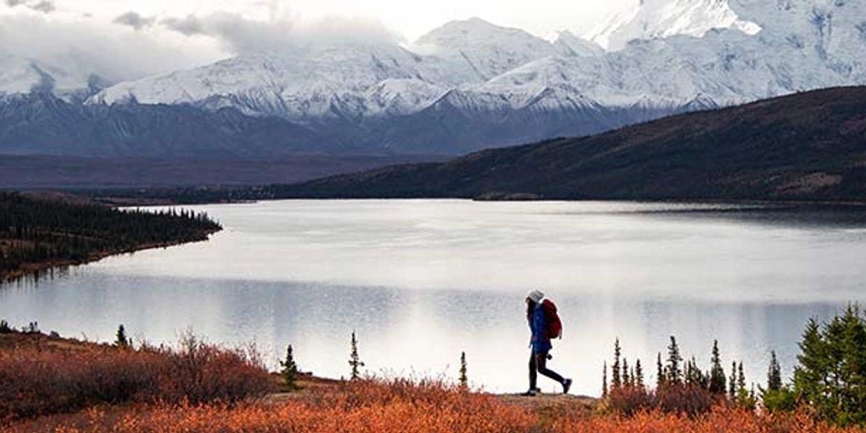 Hiker near serene Alaskan lake.