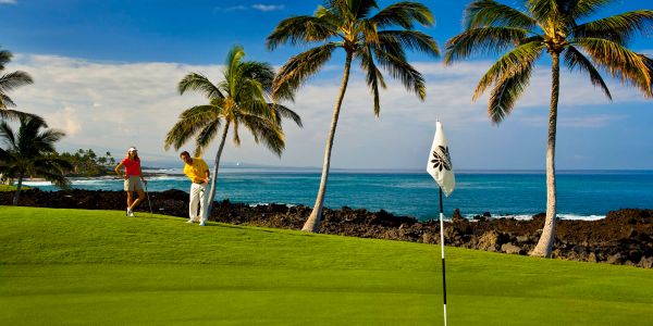Two people playing golf on a tropical course by the ocean.