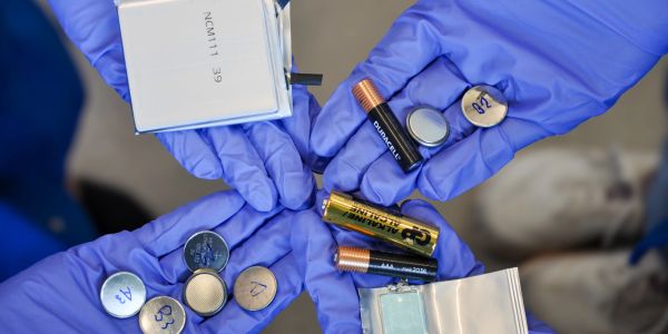 Hands in blue gloves holding various batteries and cells.