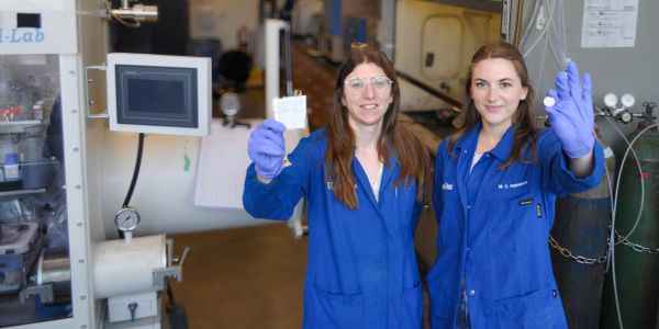Two female scientists in lab coats holding up samples.