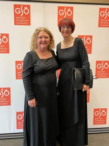 Two women in long black dresses with music folders standing in front of banner with the GSO logo in 