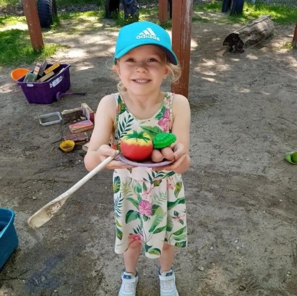 A child outside, smiling and presenting a plate full of playfood.
