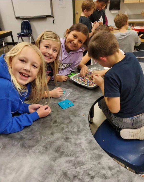 A small group of children sitting at a table smiling and working with melting beads.