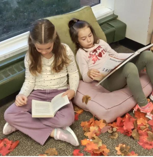 Two children sitting on pillows reading books.