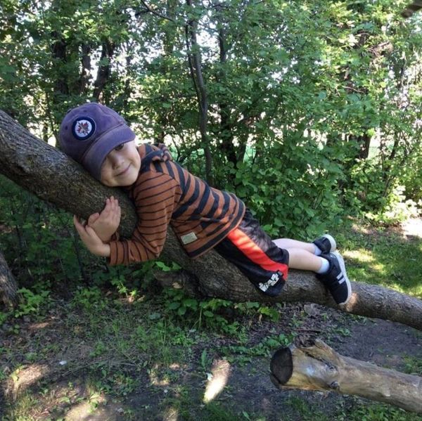 A child in the forest lying on and hugging a low lying tree branch.