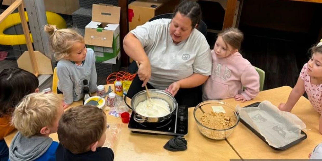 An adult doing a baking activity at a table with a small group of children.  