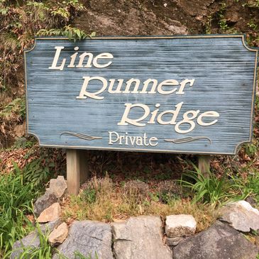 Wooden sign reading 'Line Runner Ridge Private' surrounded by rocks and greenery.