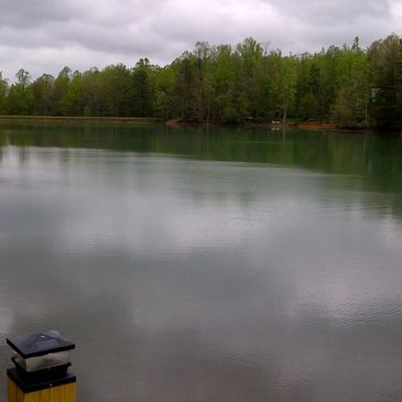 Calm lake surrounded by green trees under a cloudy sky.