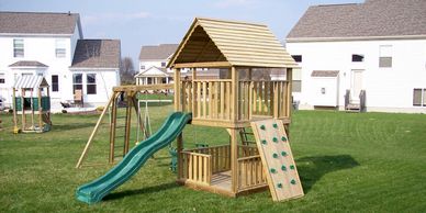 Large single tower wood playset with wood roof, rock wall, deluxe base, slide and monkey bar
