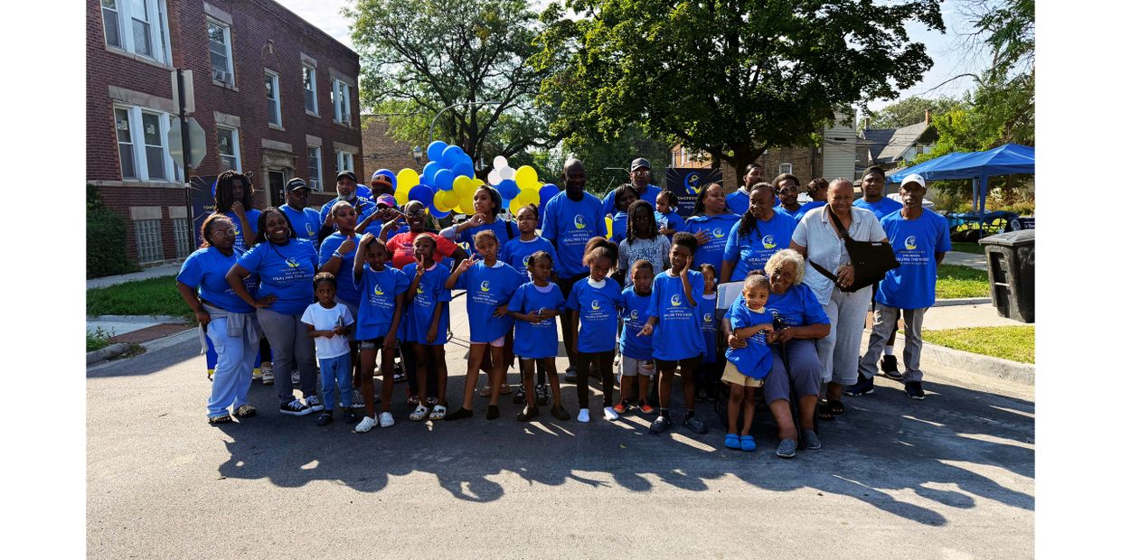 A diverse group of people in blue shirts posing outdoors with balloons in the background.