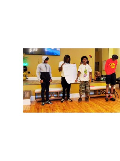 Four young men standing indoors, one holding a large sheet of paper.