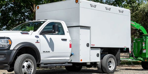 White RAM truck with utility box towing a green wood chipper in an outdoor setting.
