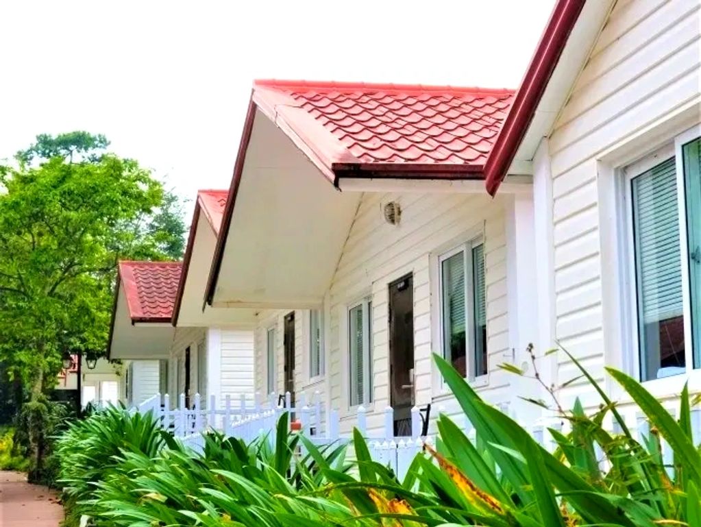 Row of white cottages with red roofs and green plants in front.