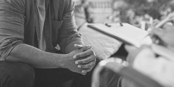 A person with clasped hands engaged in a counseling session.