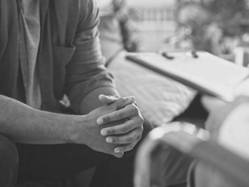 A person with clasped hands engaged in a counseling session.