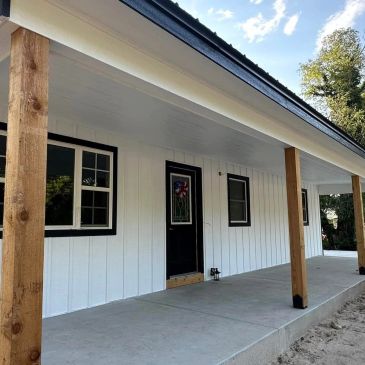 White house exterior with black door and windows, wooden pillars.